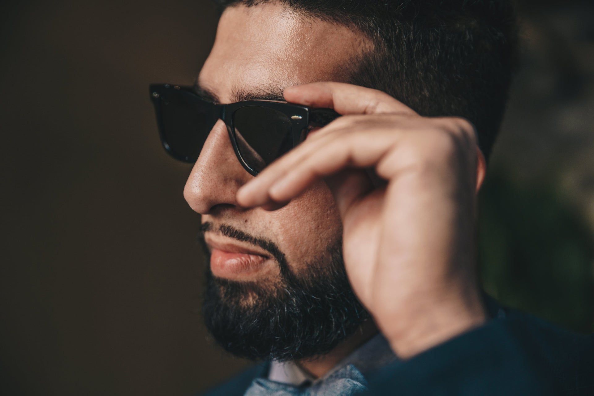 Homme ajustant ses lunettes de soleil, accessoire à nettoyer régulièrement au même titre que les bijoux