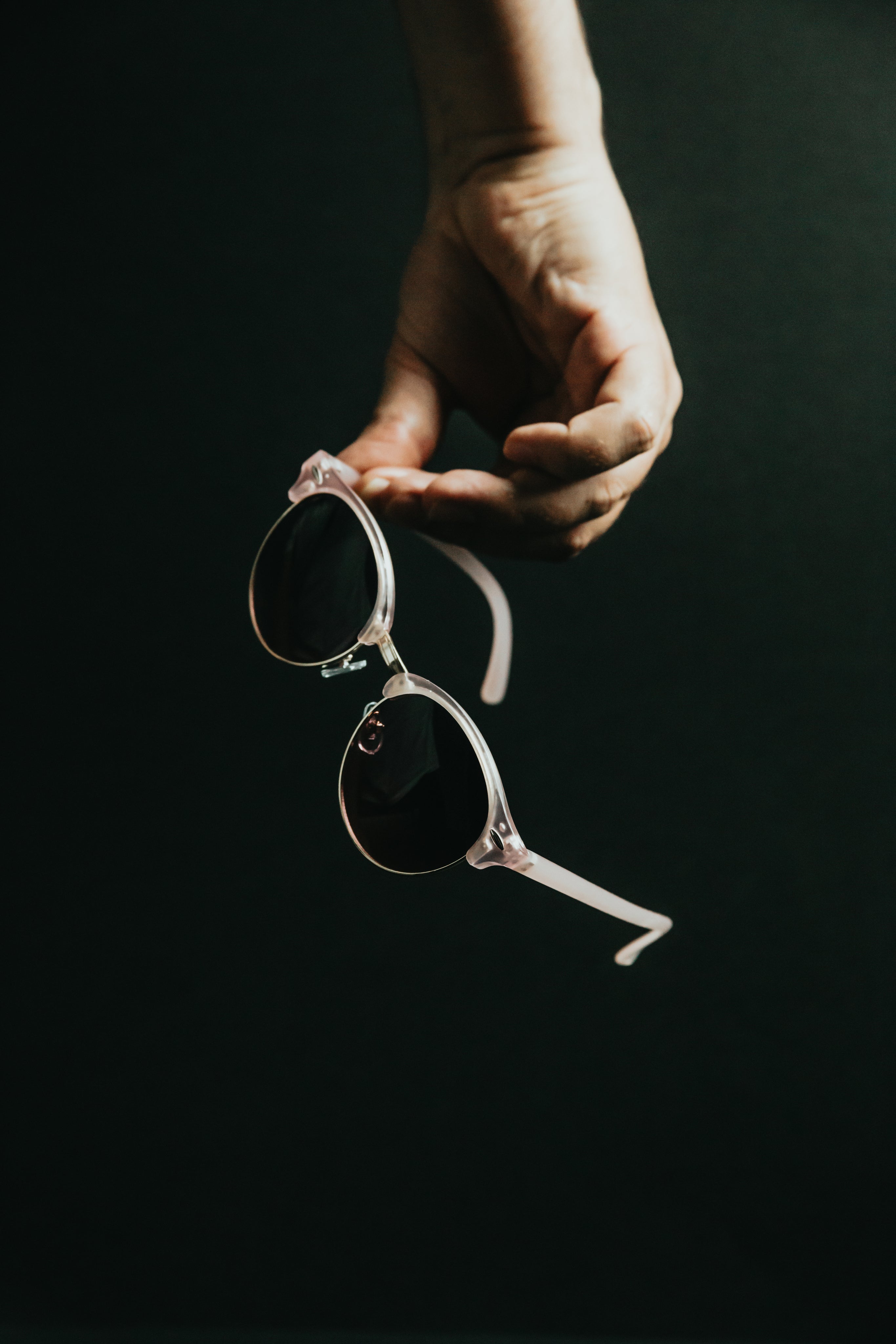 Lunettes de soleil roses tenues à la main sur fond noir, verres parfaitement nets après nettoyage à ultrasons